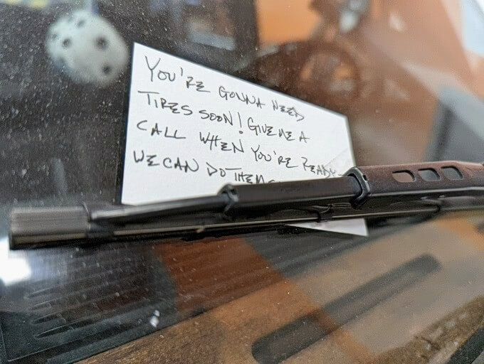 A business card with a note under a car's wiper blade.